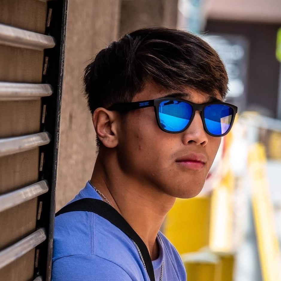 A young man in Epoch LXE - Polarized Sunglasses leaning against a wall.
