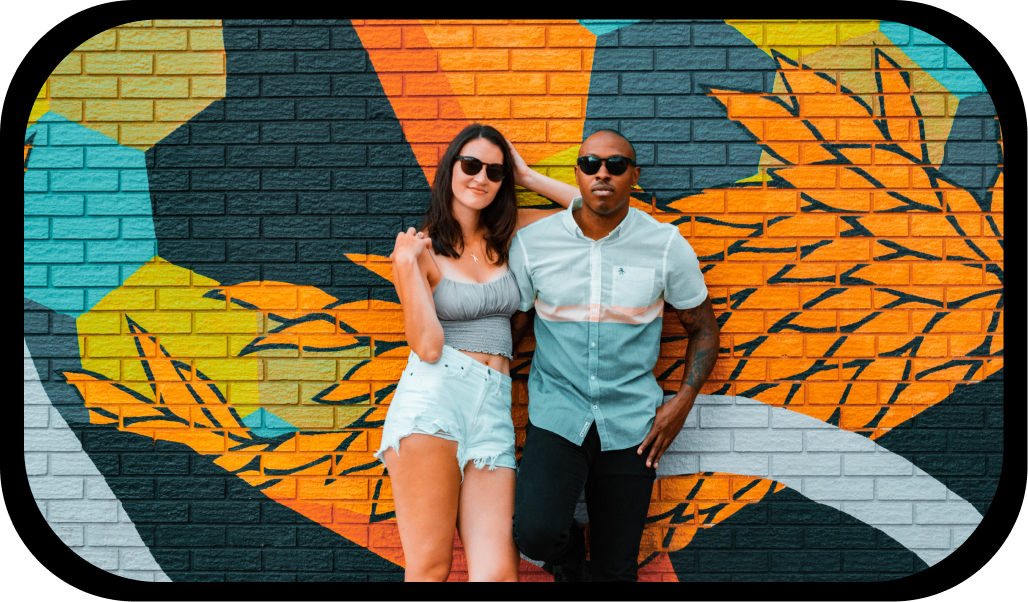 woman and man wearing sierra sunglasses leaning on art painted brick wall